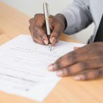 Blank man signing a lease agreement, showing just hands and a pen.