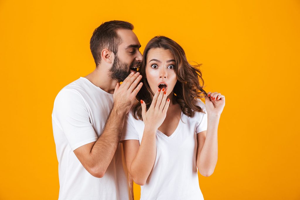 man telling a woman something in her ear, plain background.